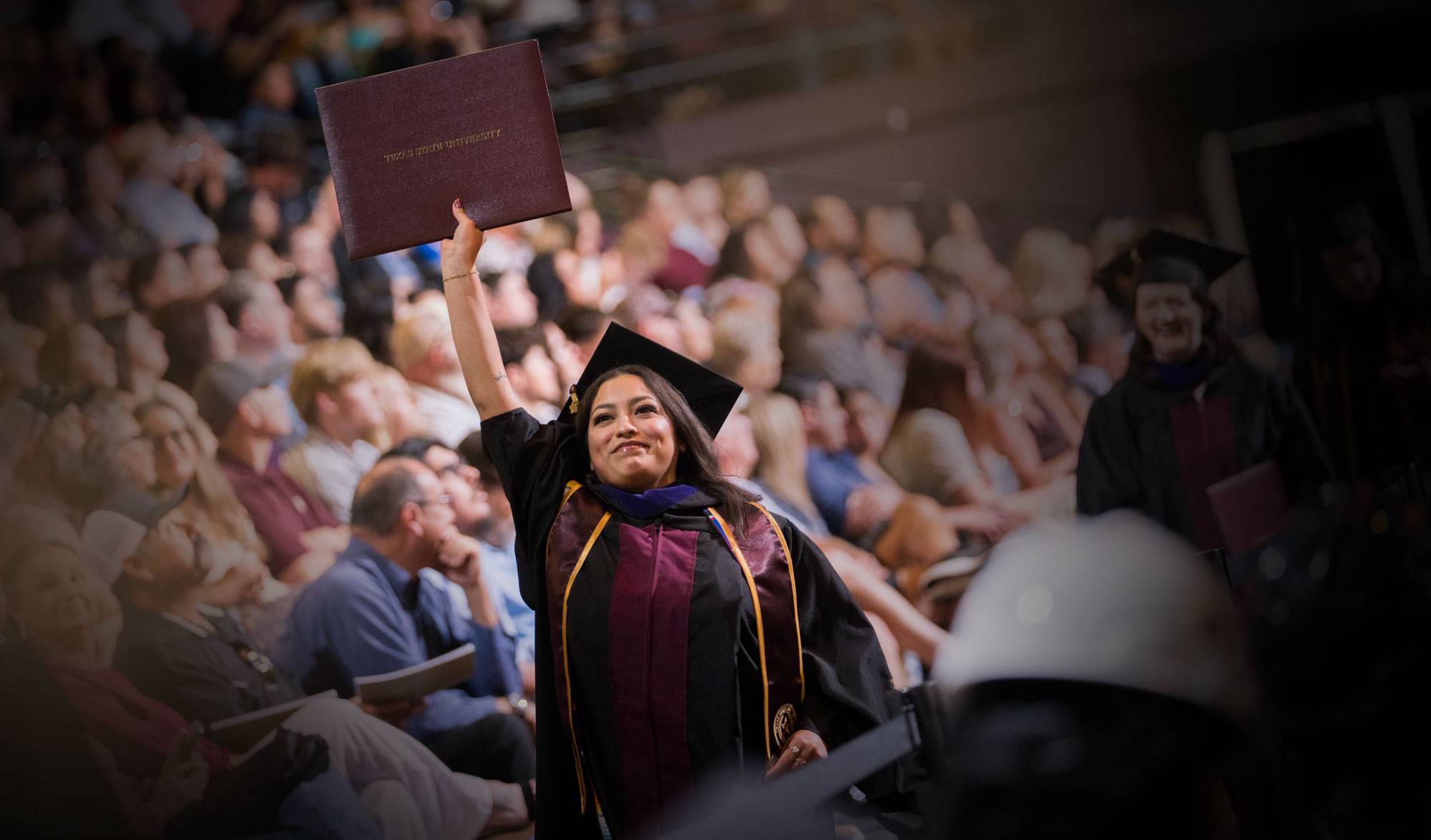 Female graduate at commencement holding her diploma high in her right hand