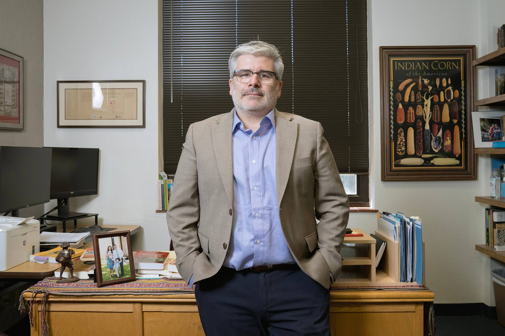 Dr. José Carlos de la Puente, wearing a dark tan blazer, sits against his desk in his office.