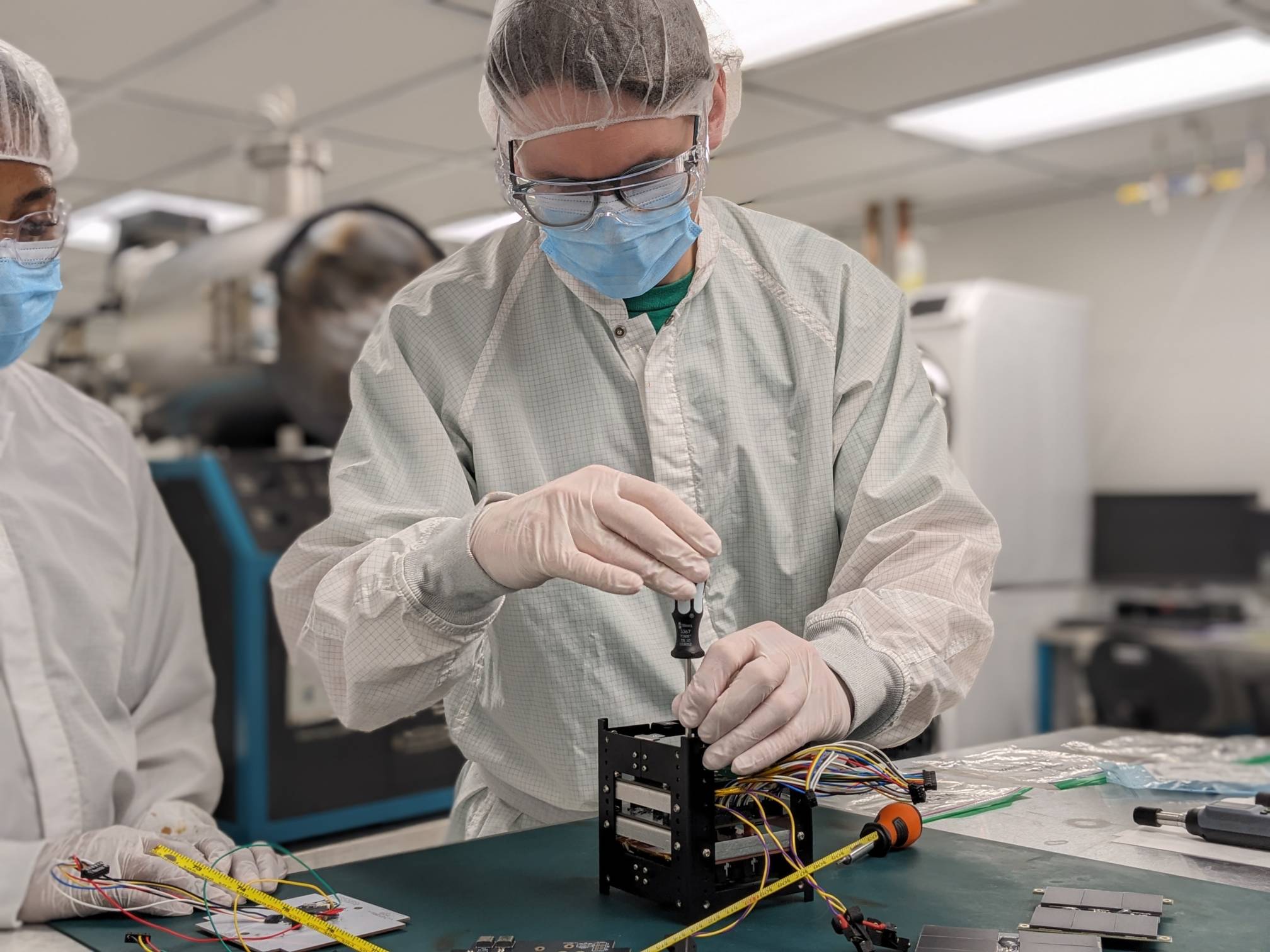man in white lab coat uses screwdriver on a black cube box