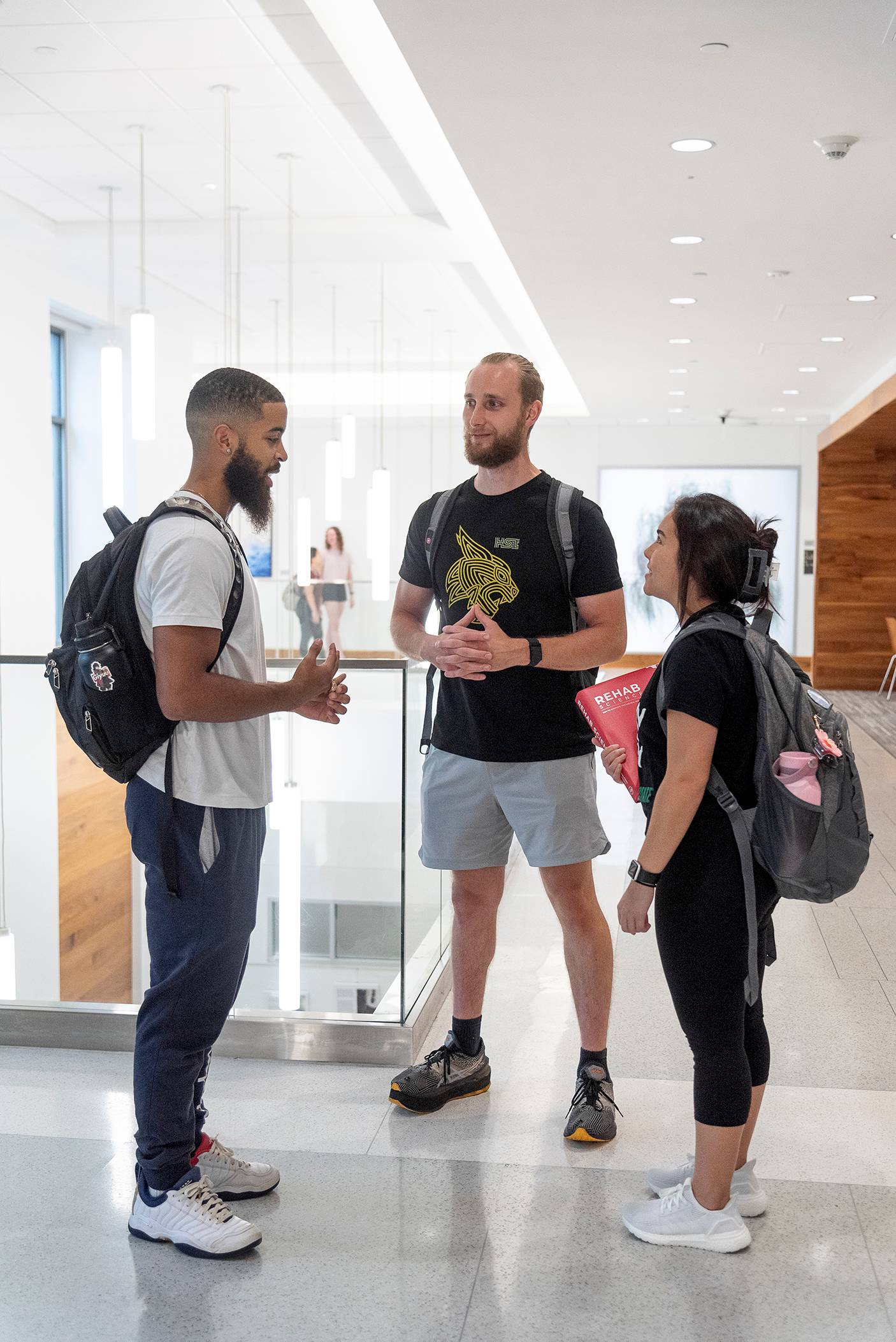 three students standing in bright hallway conversing