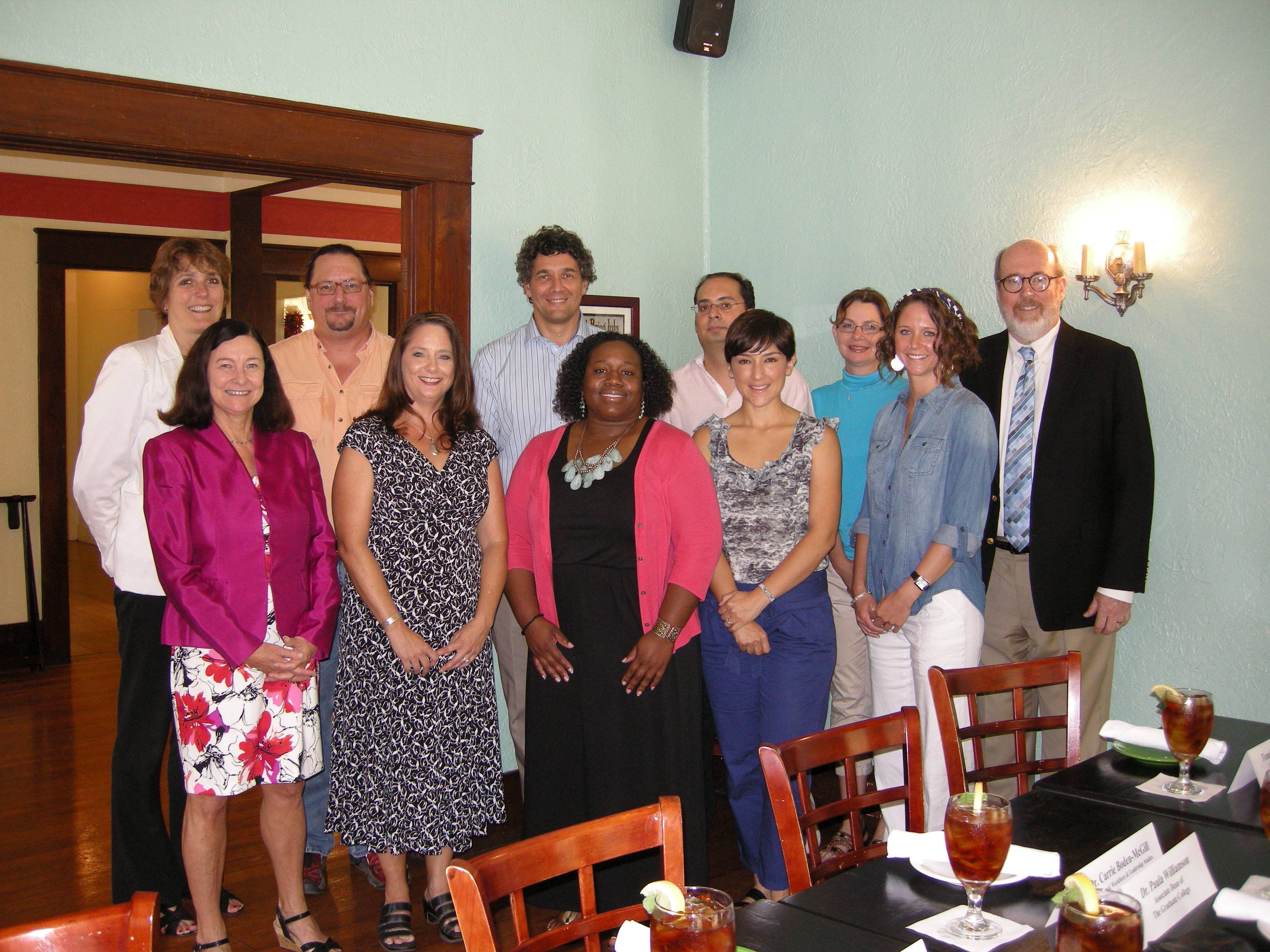 group photo of 11 people. they are in a pale blue room and standing behind a table with chairs