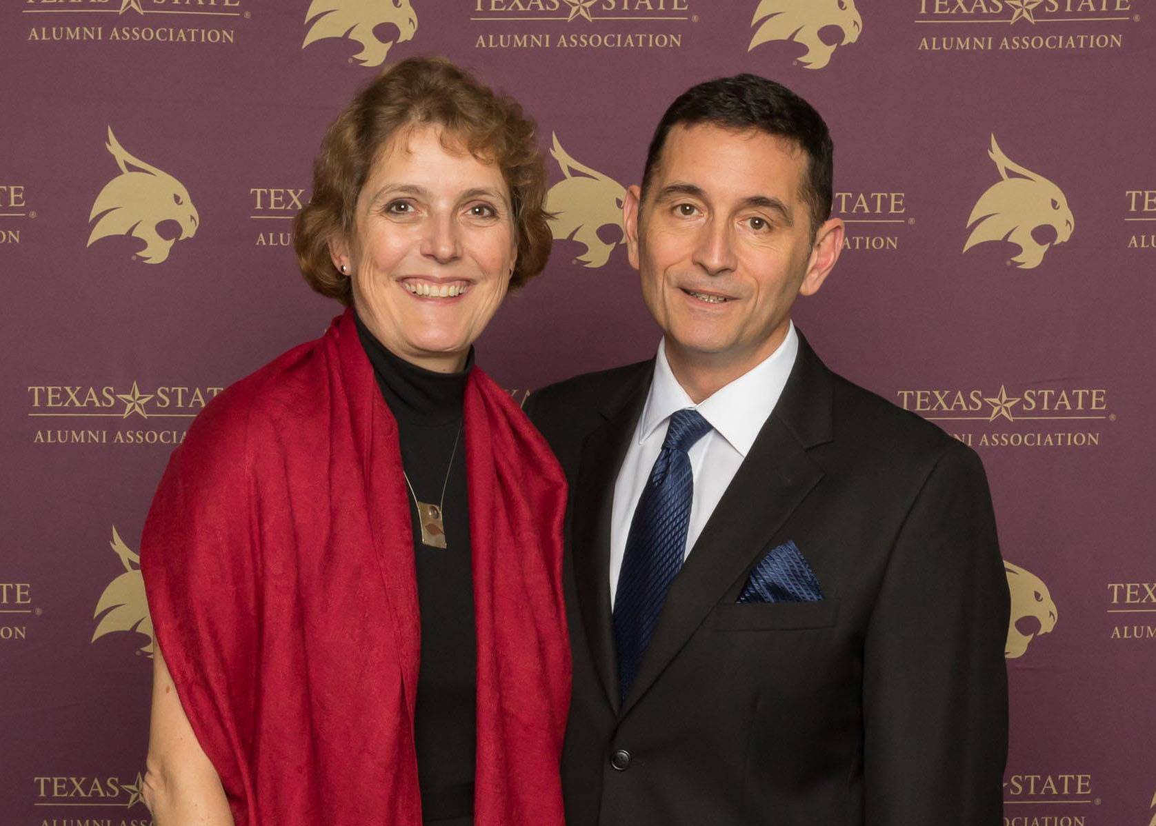 woman and man pose for photo in front of txst-themed step and repeat