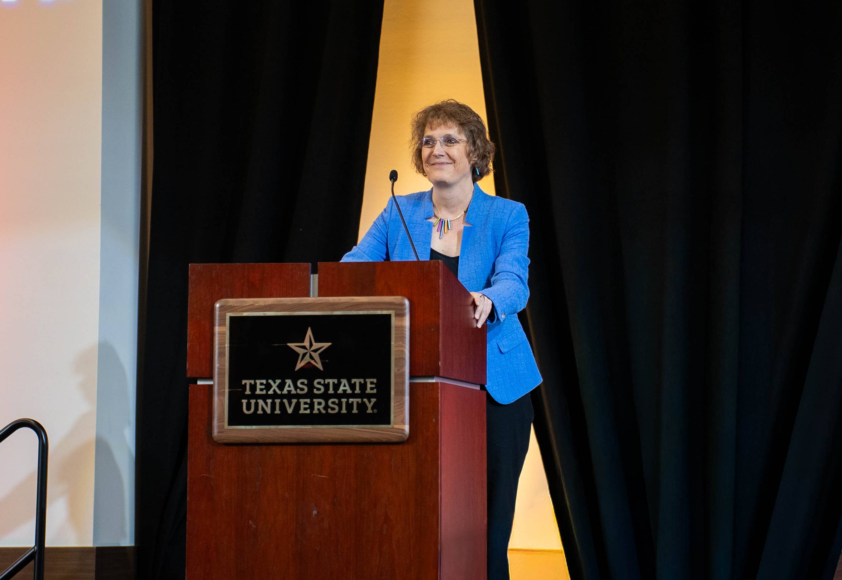 woman in bright blue blazer standing behind wooden podium
