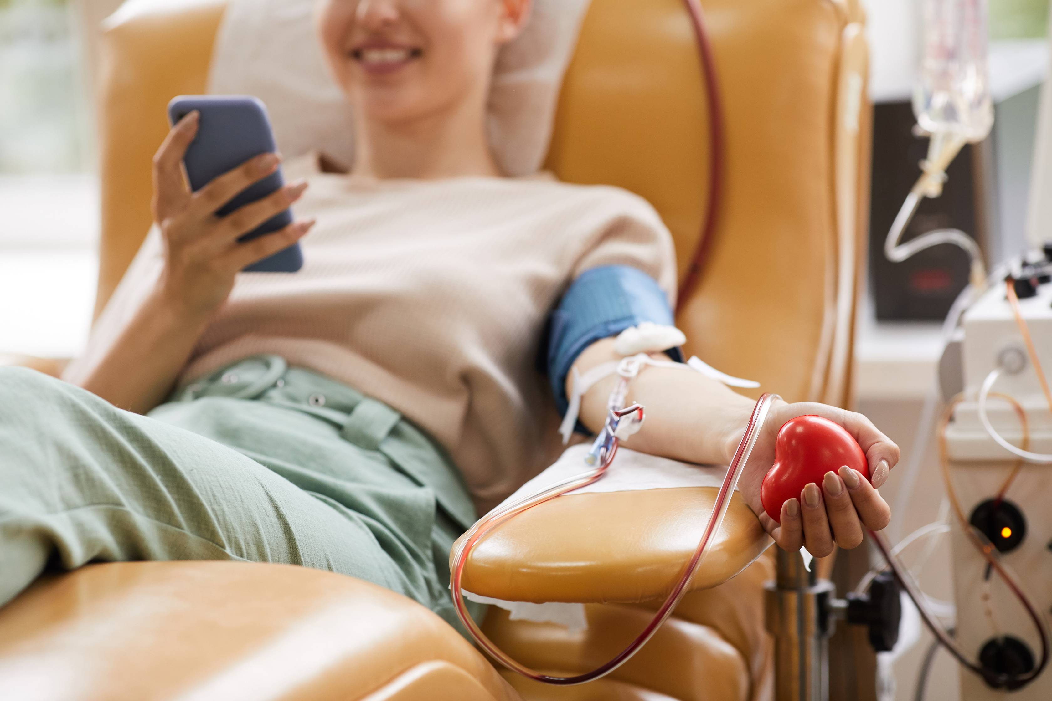 woman donating blood while laying in brown chair and playing on phone