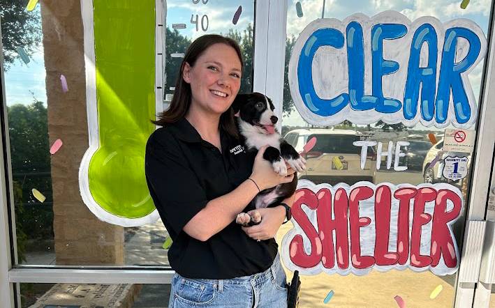 woman holds up small black and white dog outside animal shelter