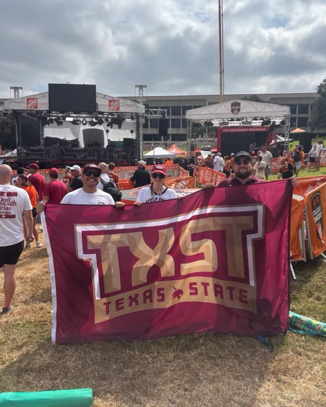 Three Texas State fans holding up a TXST flag in front of the College Game Day stage