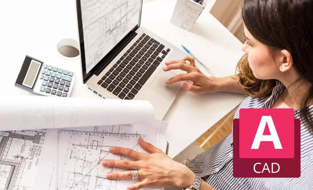 a woman looking at blueprints and working on laptop at desk
