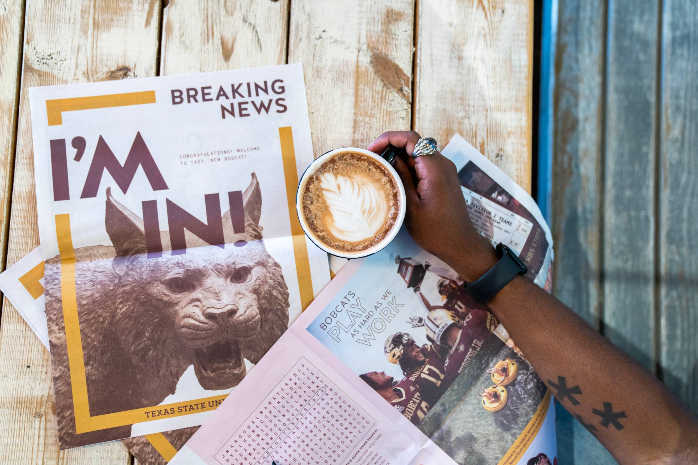 Newspapers on a table with a coffee mug featuring foam latte art