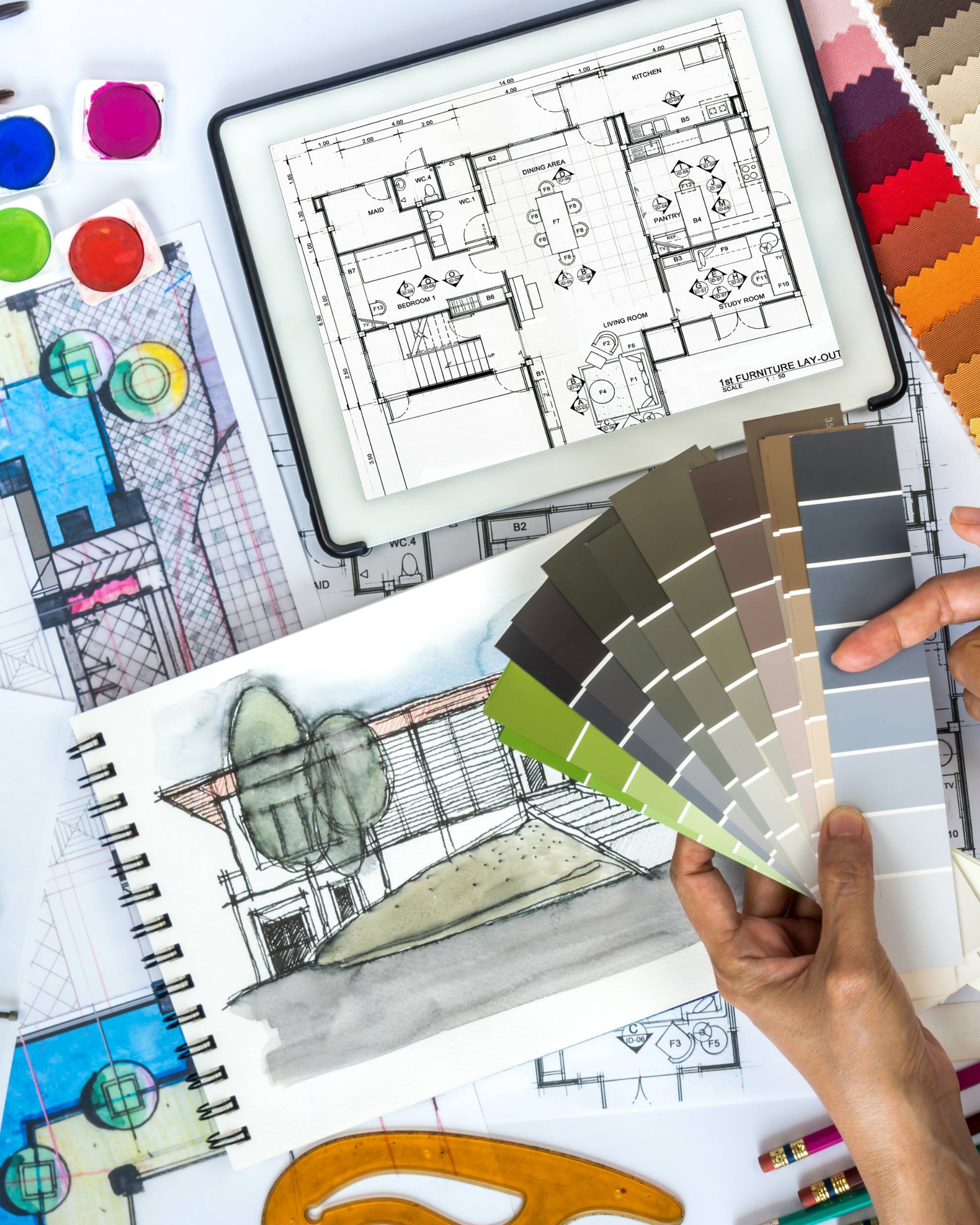 a person holding paint samples over a desk full of ipads and design elements