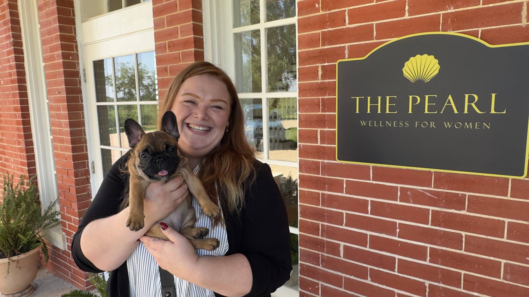 woman holding small brown french bulldog next to brick building