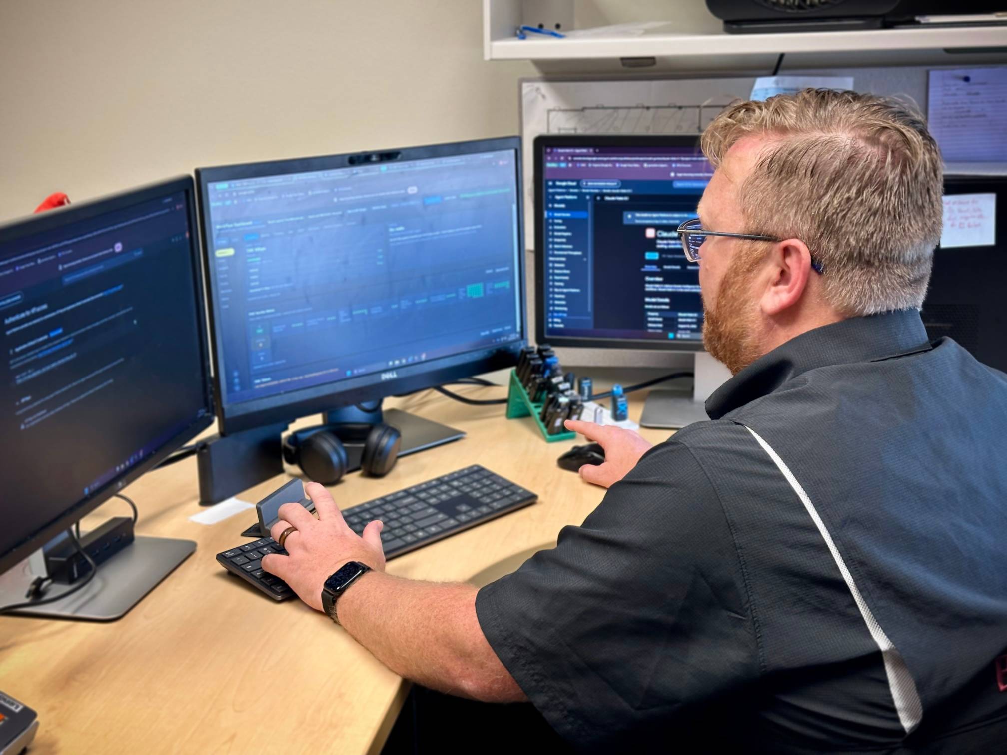 A person seating at the desk with three computer monitors