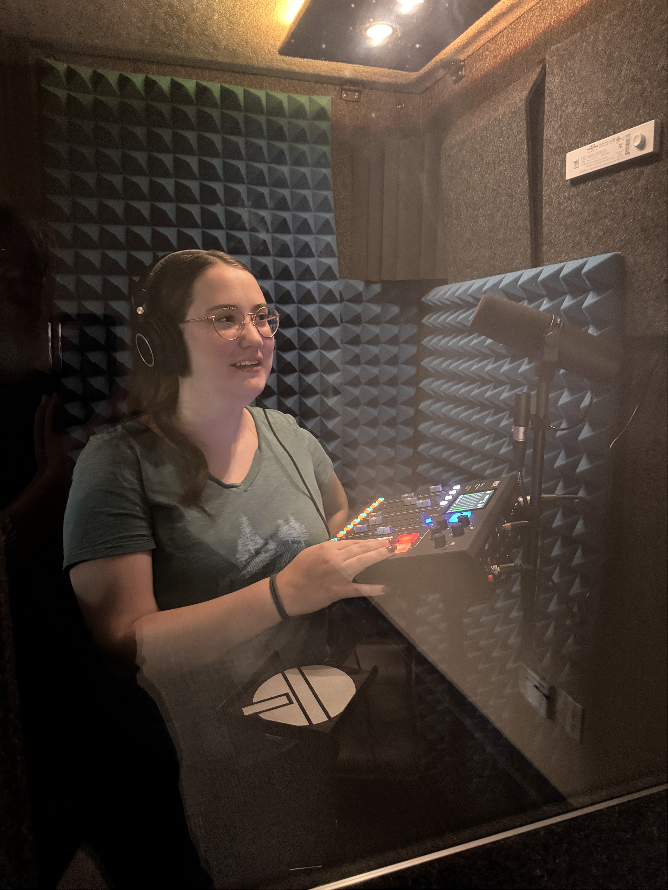 A podcast recording setup with a microphone, mixer, headphones, and lamp on a wooden table, accompanied by two chairs