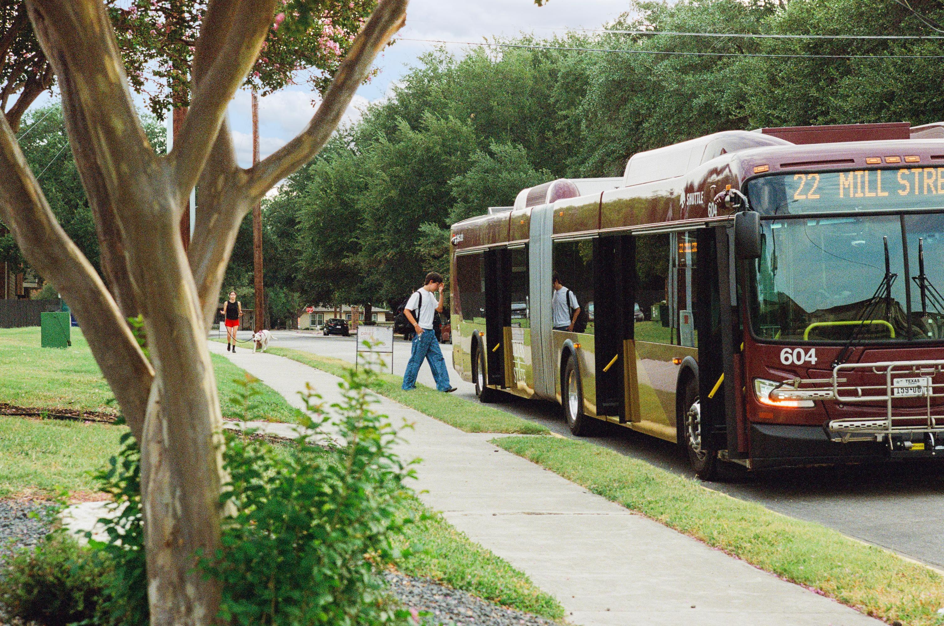 man in white shirt and jeans boards a large maroon TXST shuttle bus