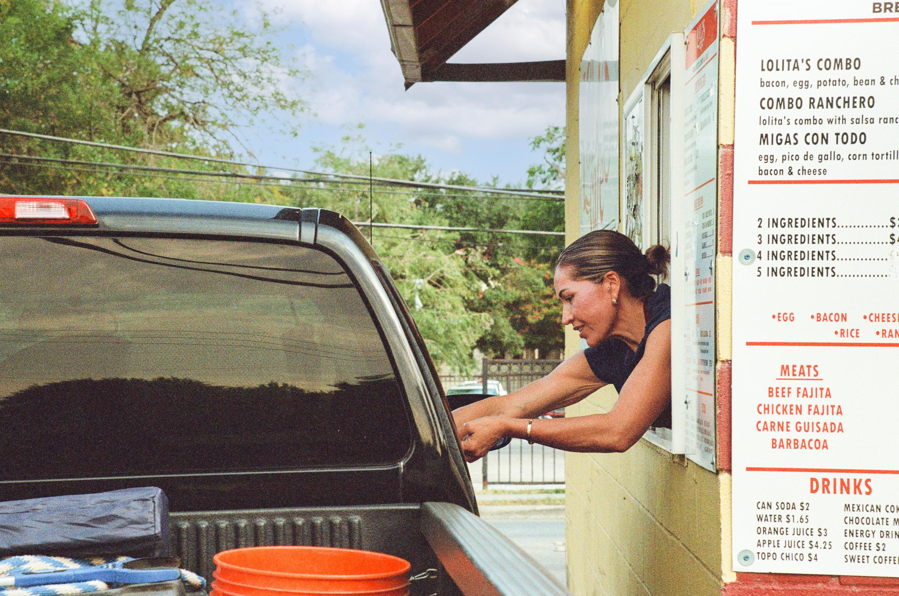 woman leans out of drive-thru window to hand money to black truck