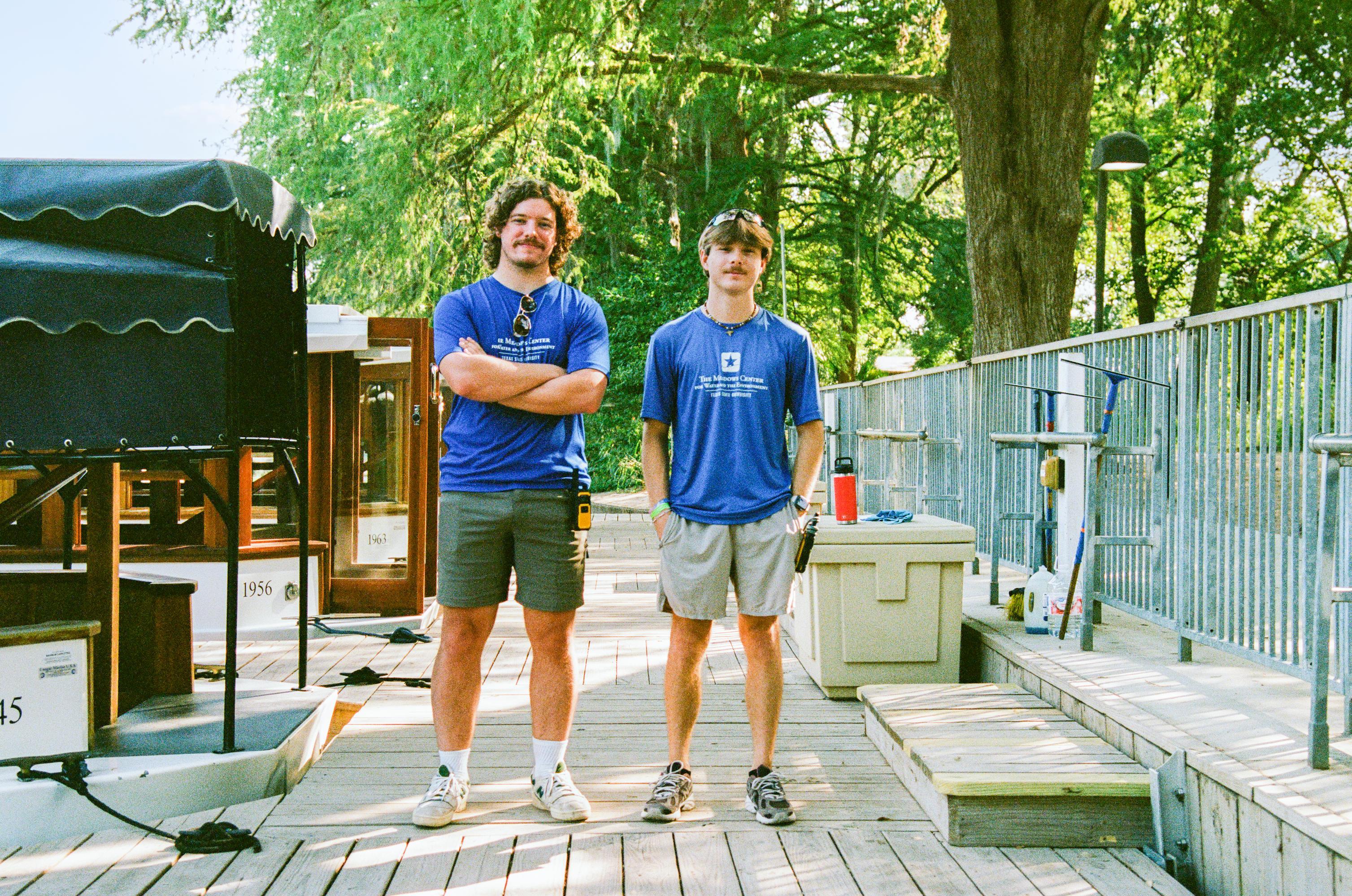 two men in blue shirts and shorts stand on deck at The Meadows Center and pose for photo. 