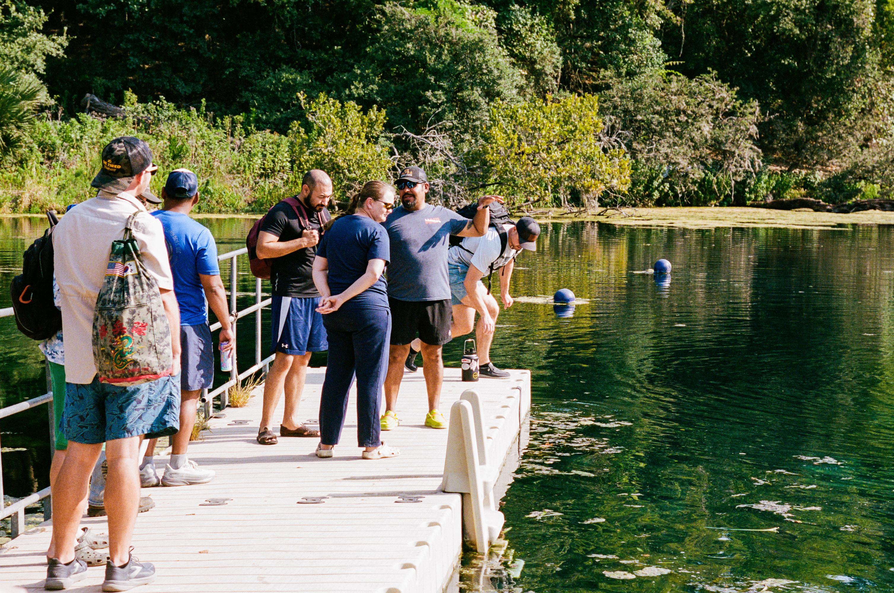 Large group of people stand on deck and look into spring-fed river below them