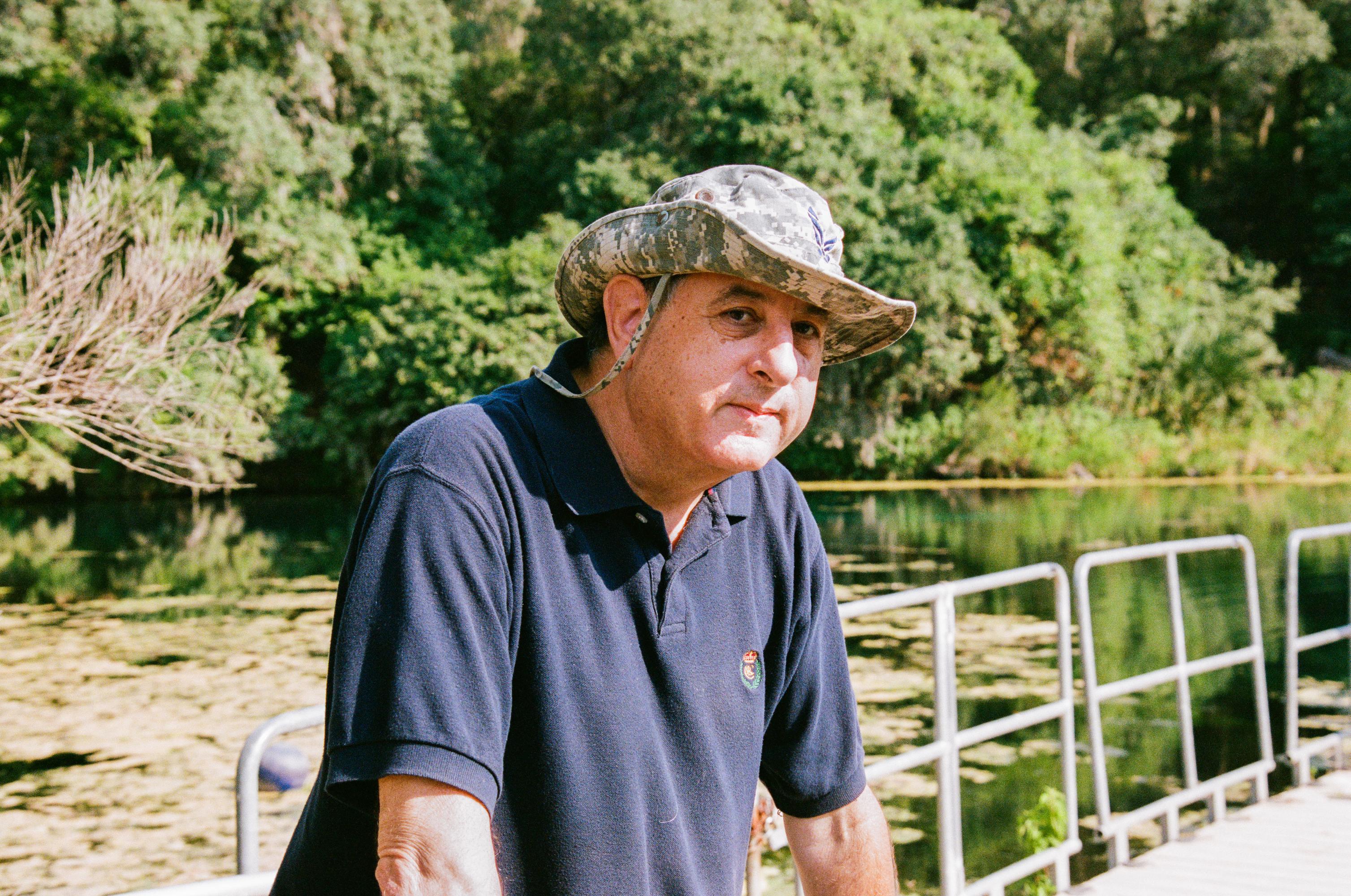 man wearing a camouflage bucket hat and navy polo shirt looks off into the distance
