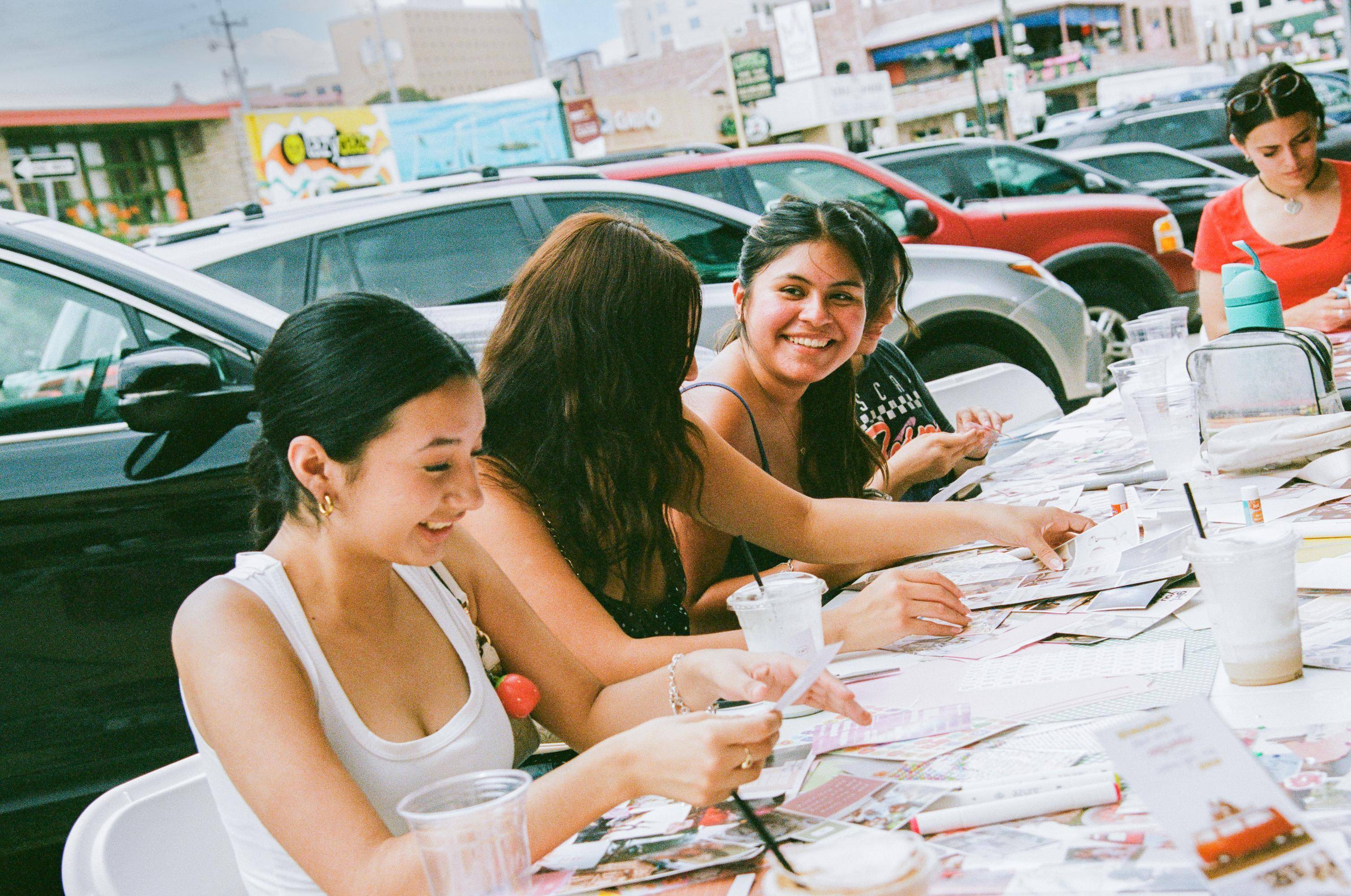 multiple woman sit at a table outside while they are scrapbooking