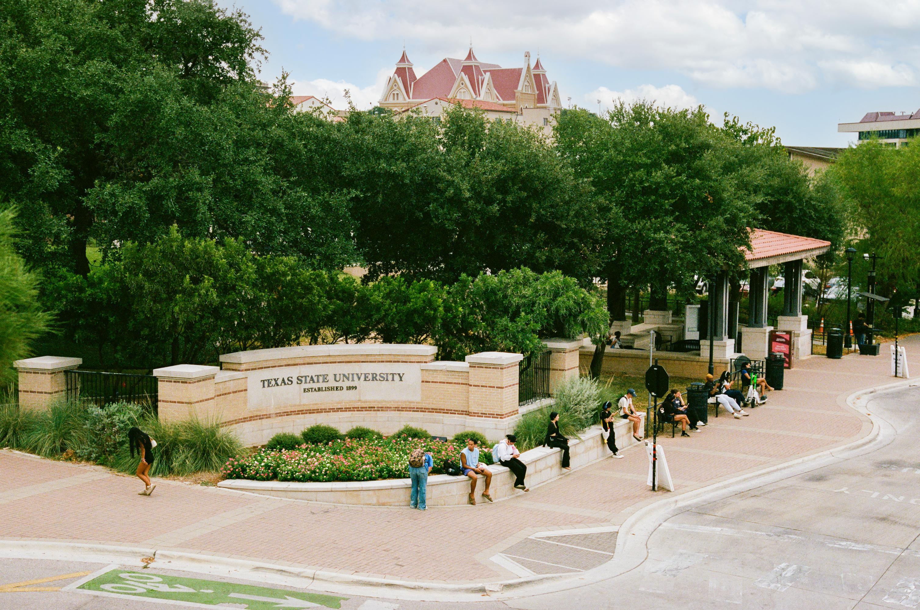 aerial view of people waiting at a bus stop next to large Texas State University sign