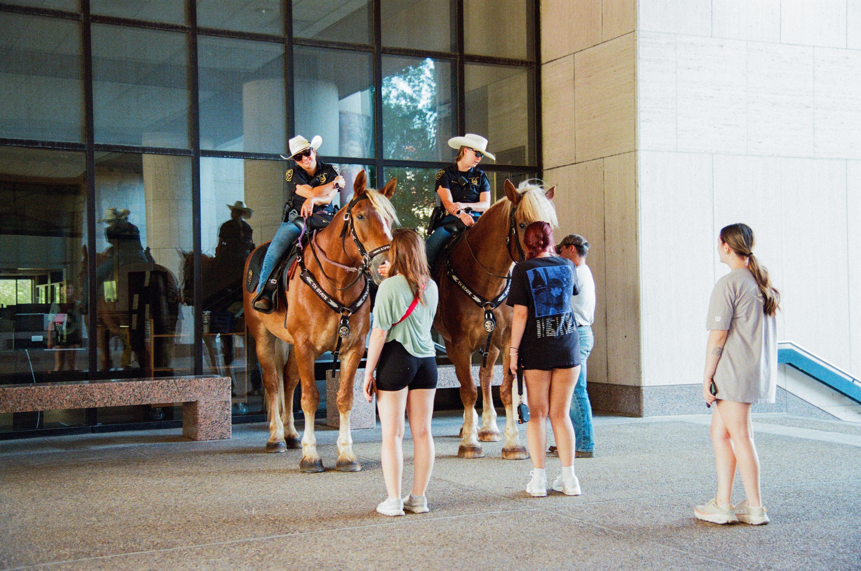 female students pet large horses while police offers sit on the horses. 
