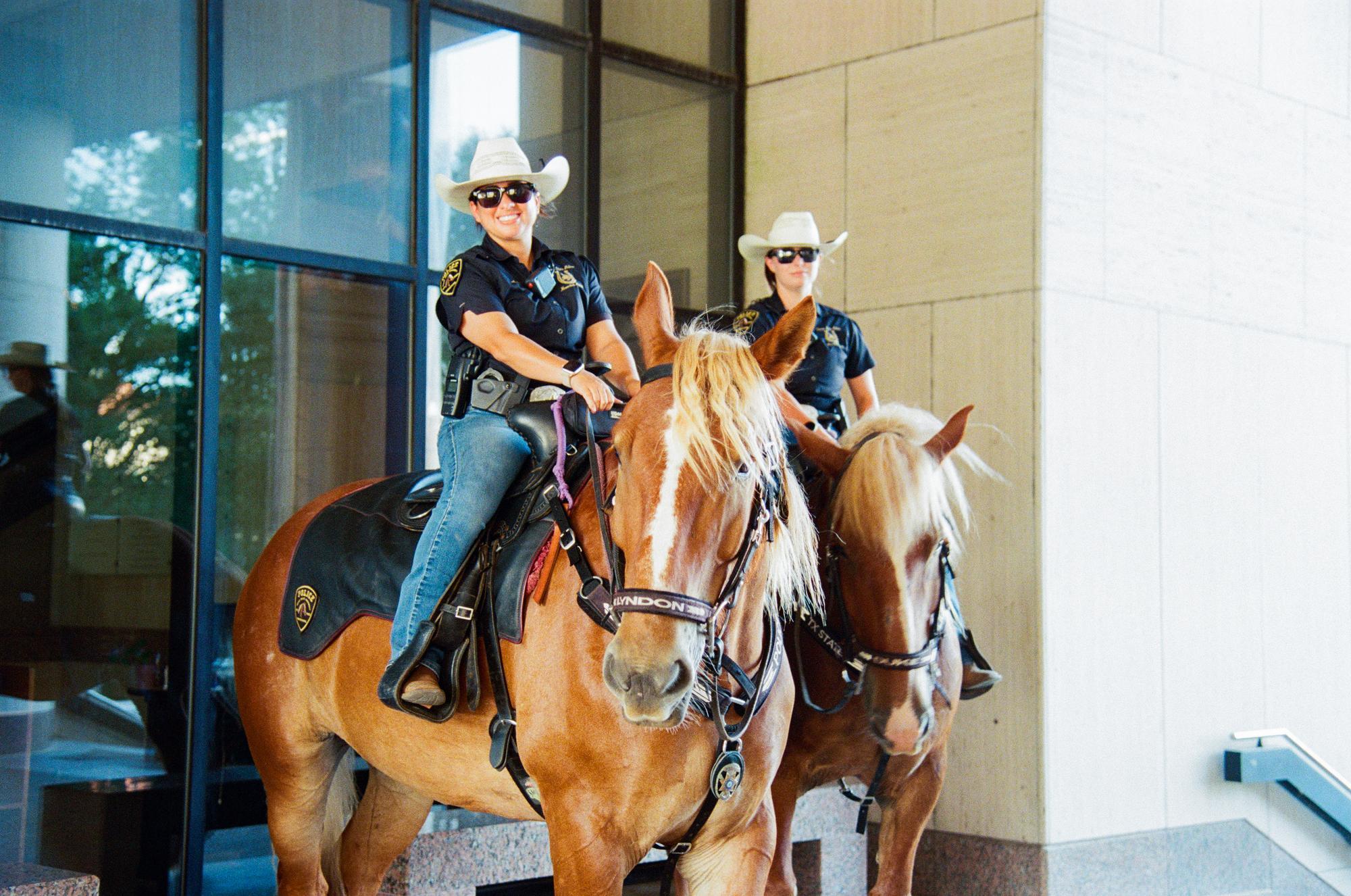 two police officers in cowboy hats sit on large brown horses in front of large windows