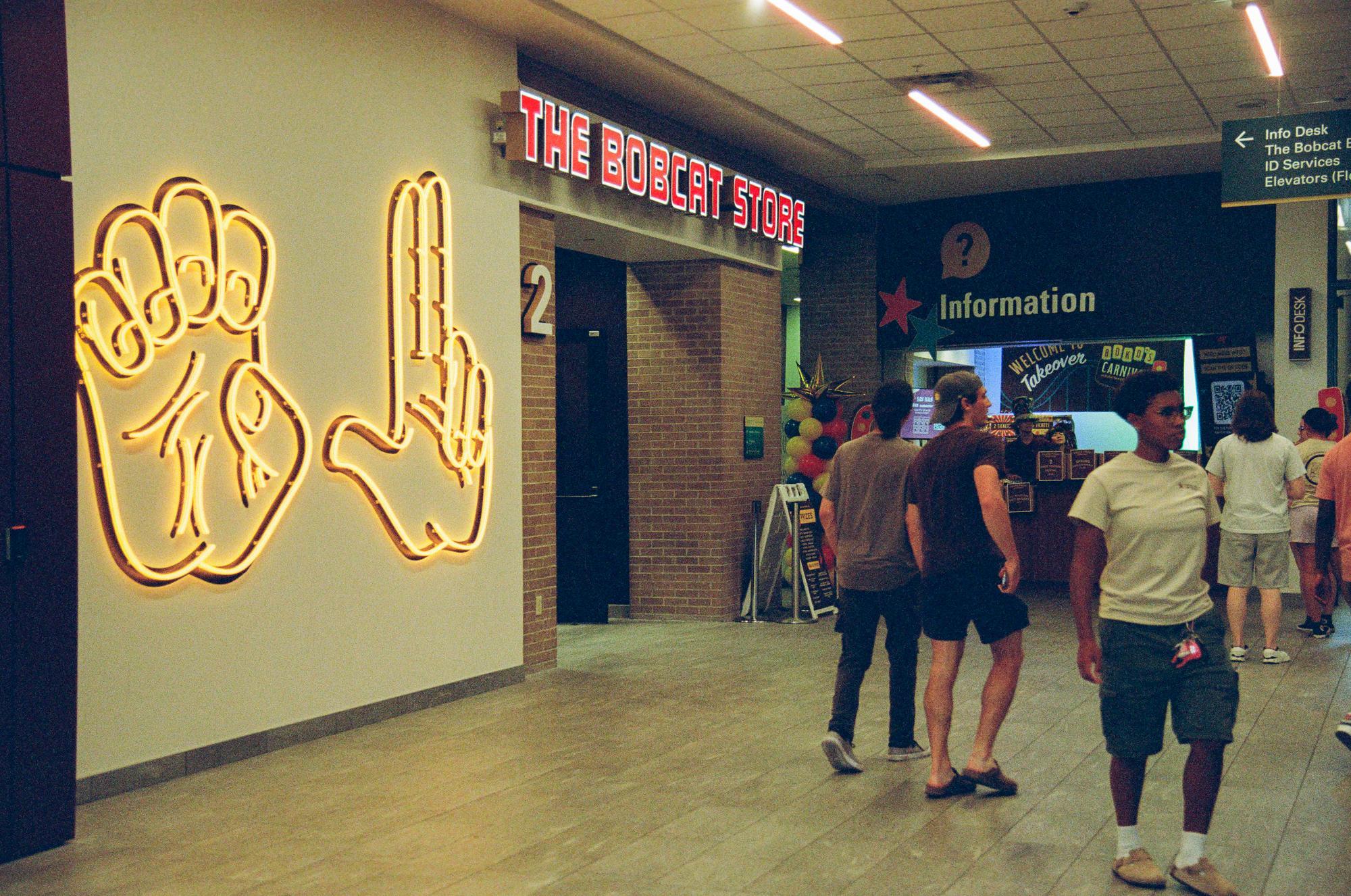 group of students walk in lobby next to large neon signs of the TXST hand signs. 