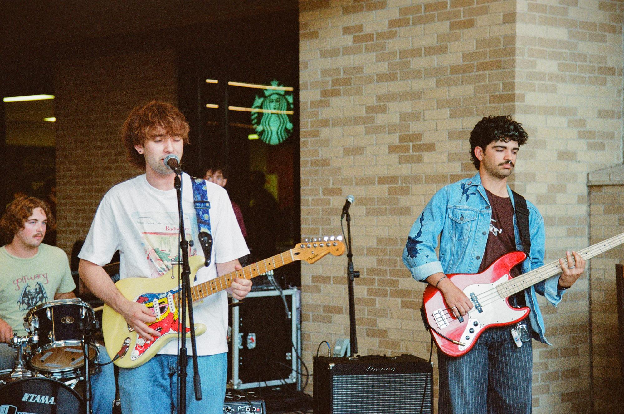 three men in a band playing instruments. the guitarist is singing into a microphone. 