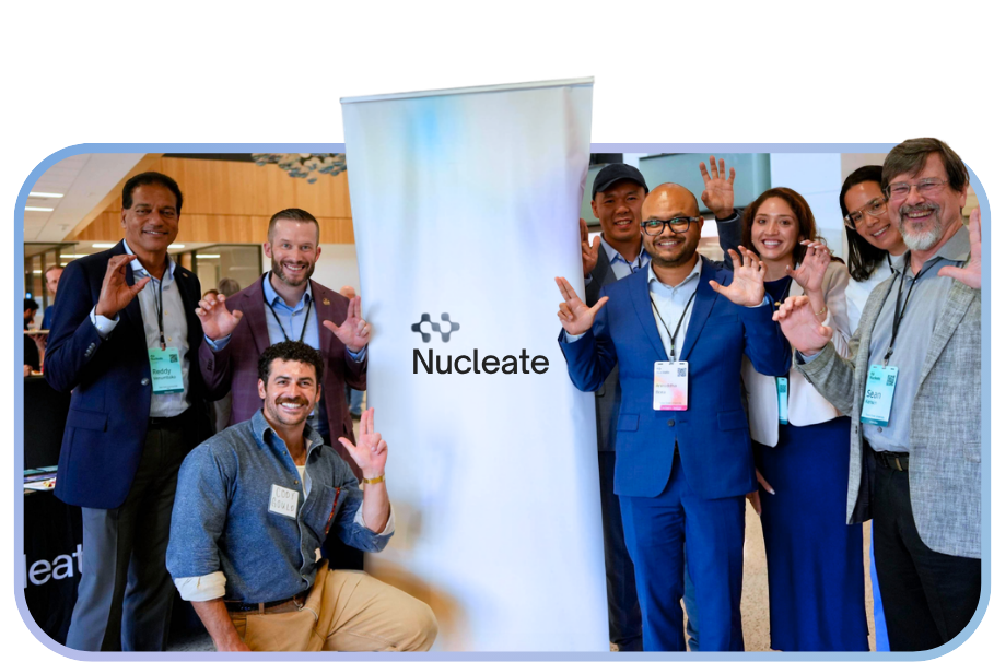A group of Nucleate members posing together and smiling in front of a Nucleate banner, wearing professional attire and conference badges.
If you'd like a shorter version for tighter character limits: "A smiling researcher in a lab coat standing in a laboratory with equipment behind him.