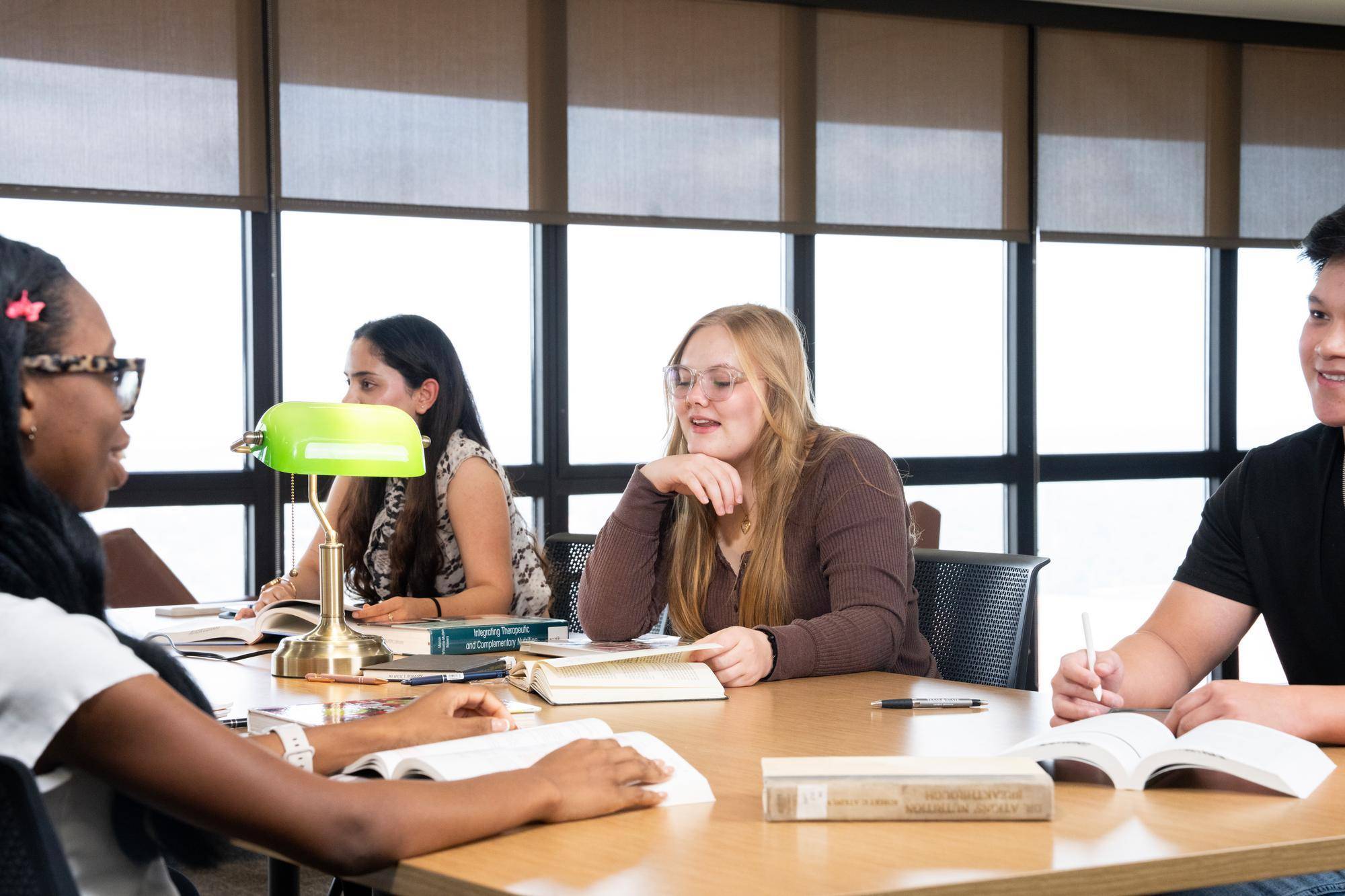 four students sit around a wooden table conversing