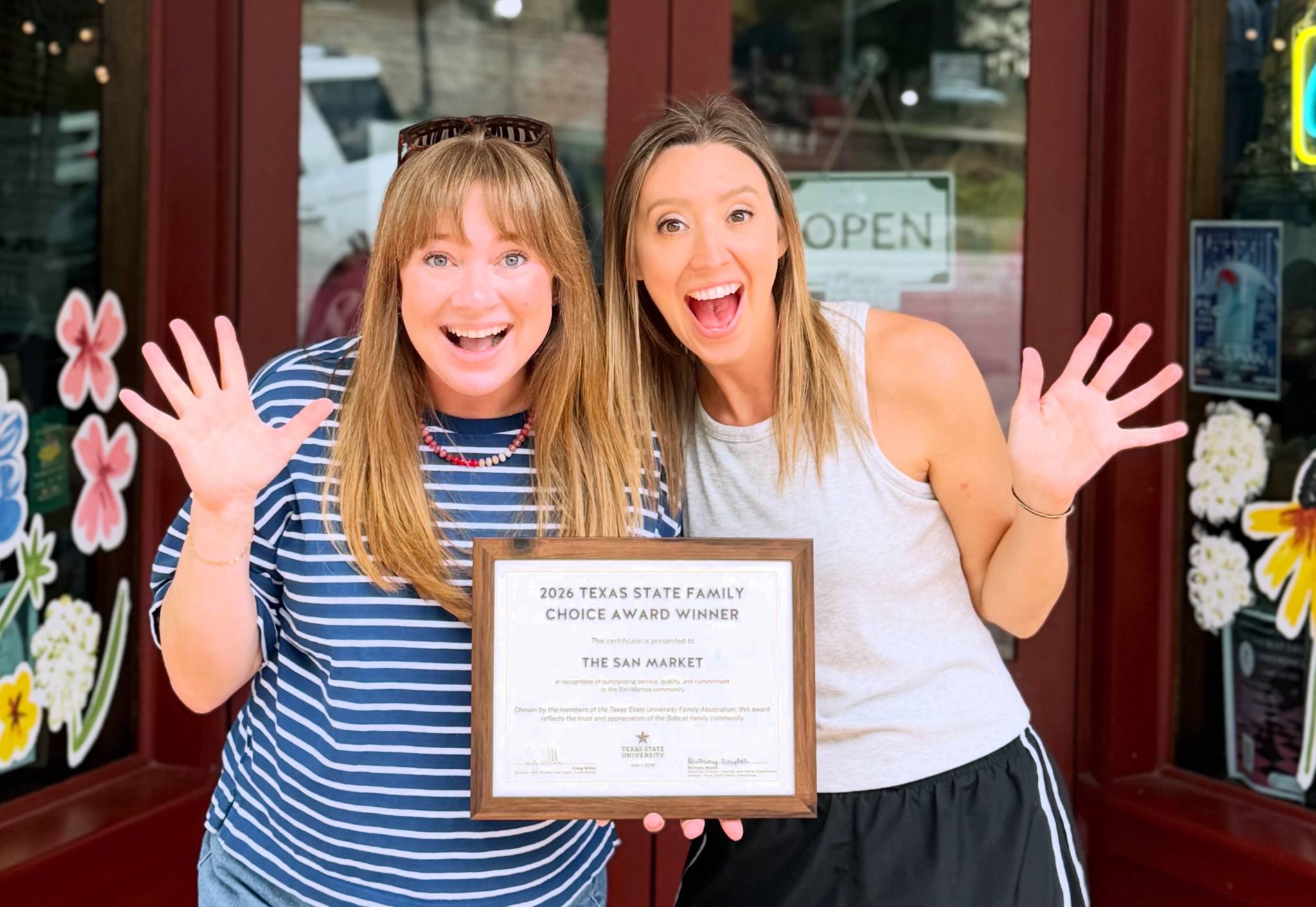 Two women posing with an awards certificate with their hands out in excitement