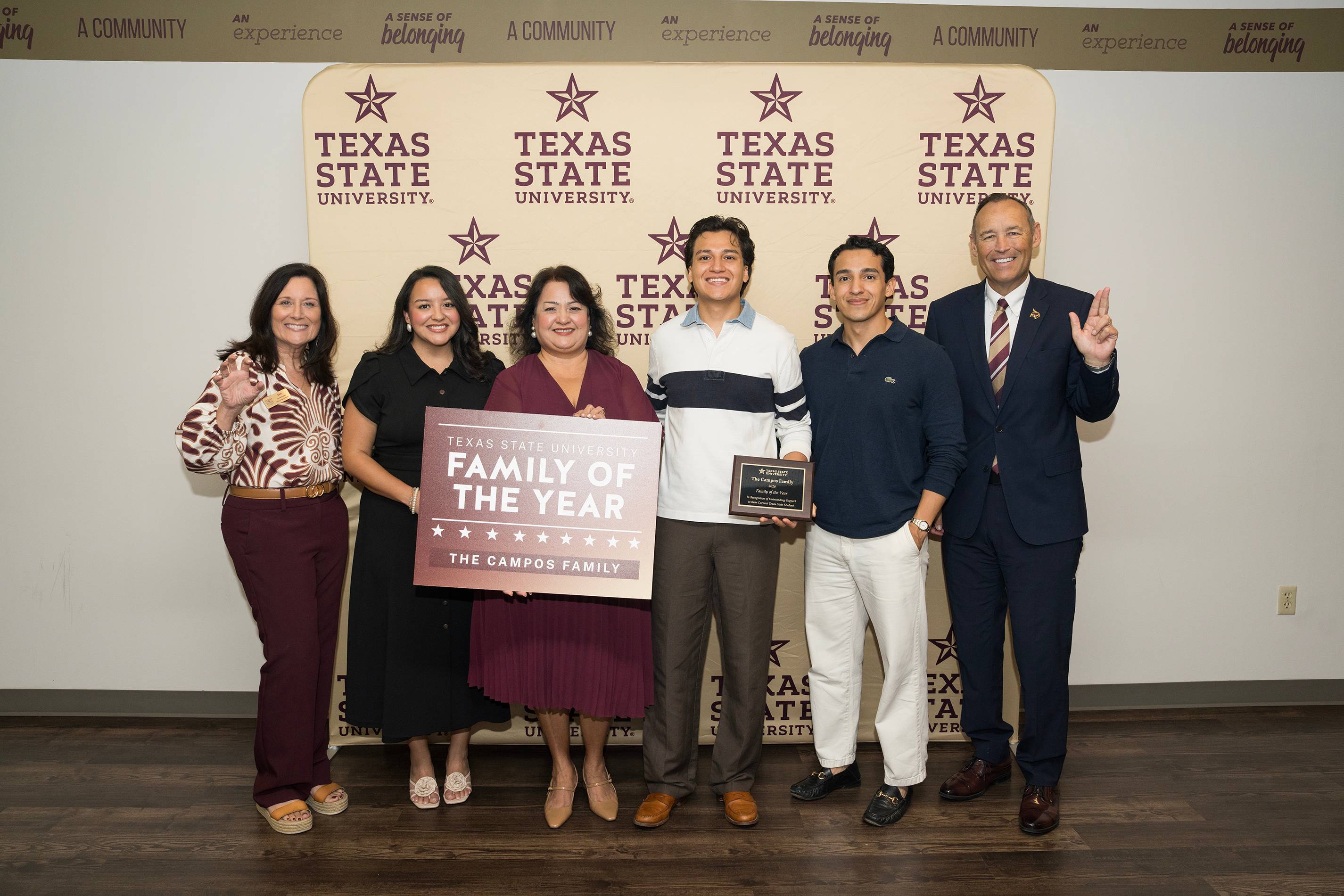 six people pose for photo while holding up sign reading "Family of the year" 