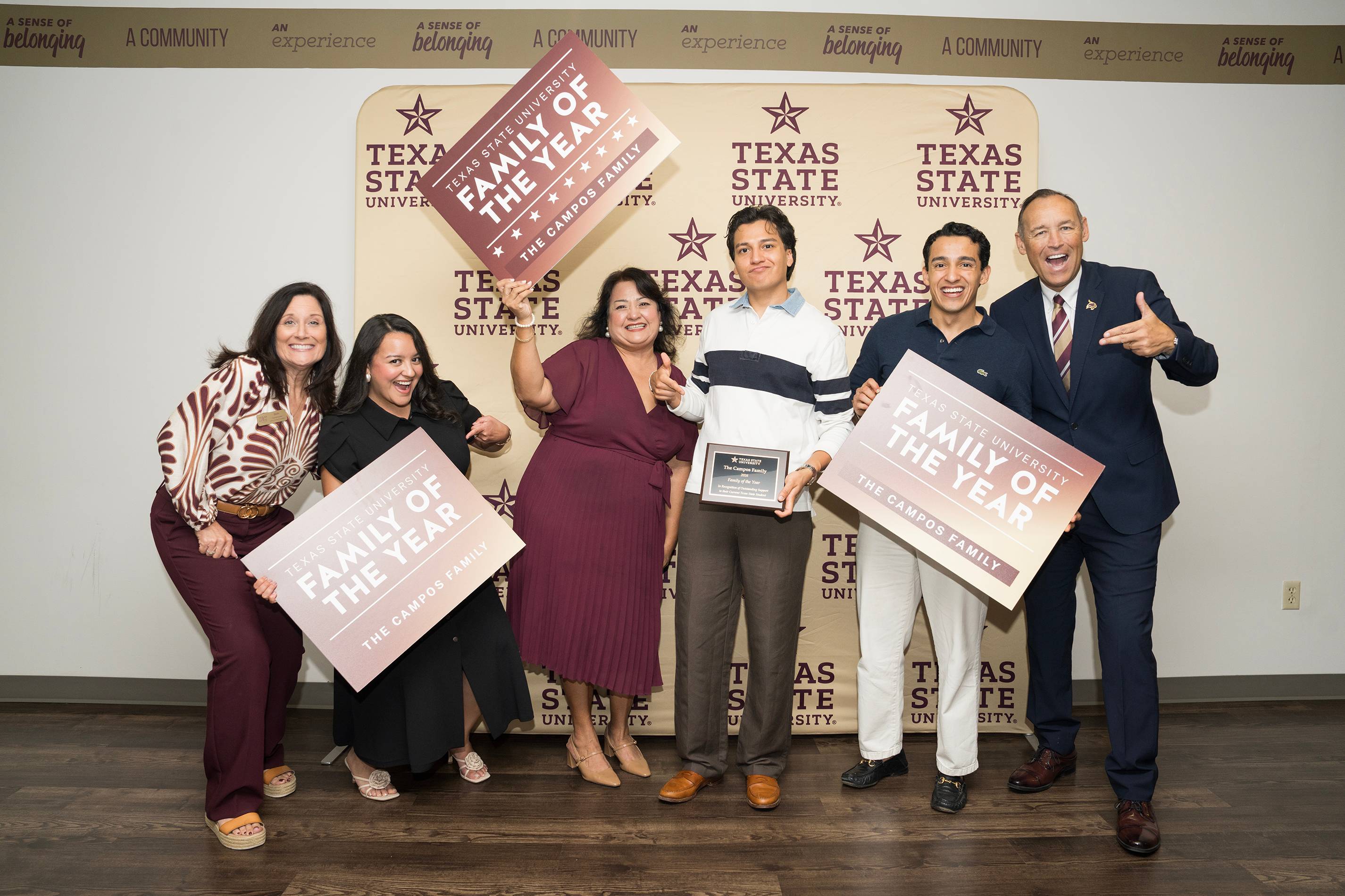 six people make silly poses with large "Family of the Year" signs