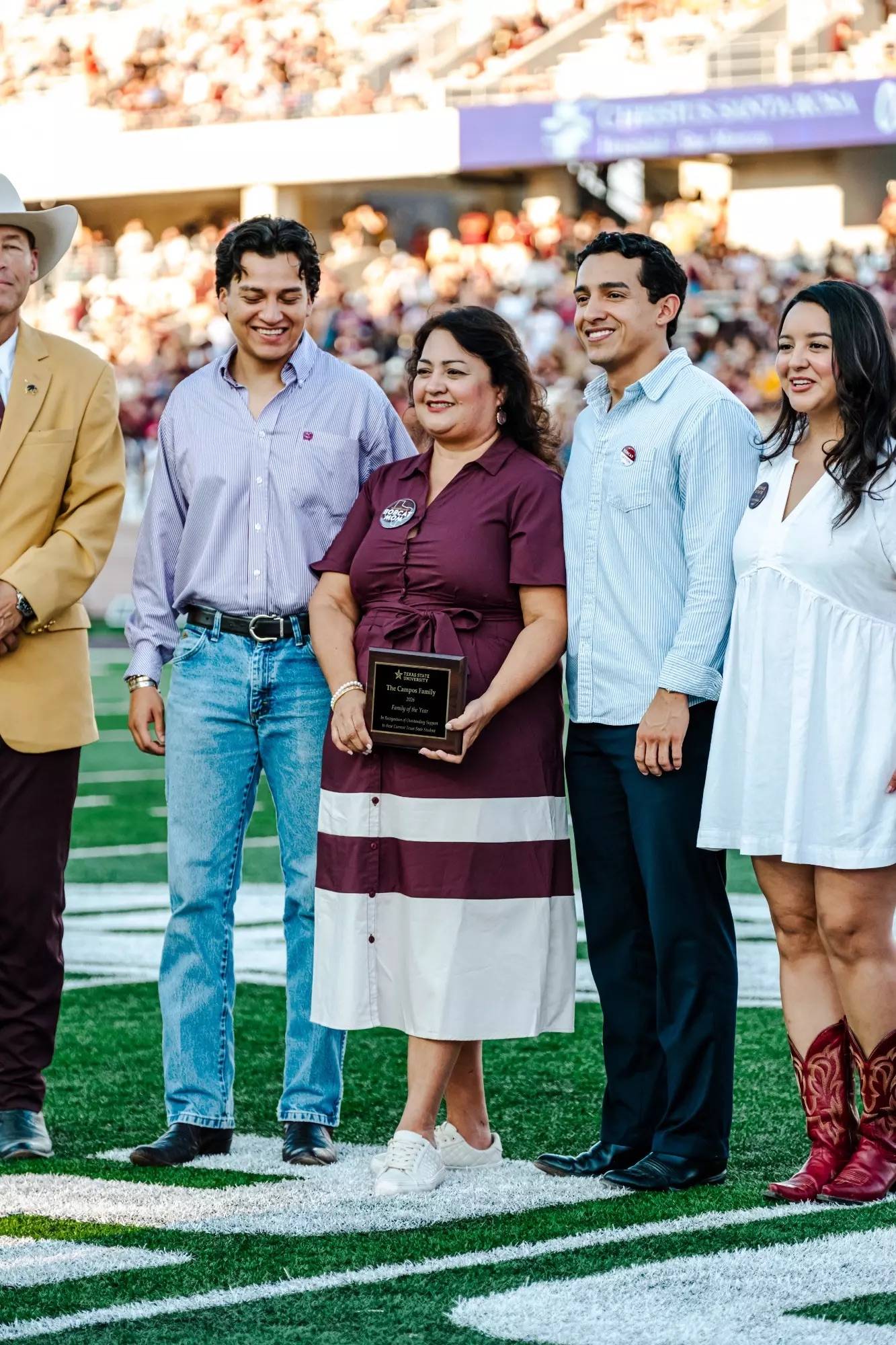 two women and two men pose for photo on football field. one of the women is holding a wooden and metal award plaque. 