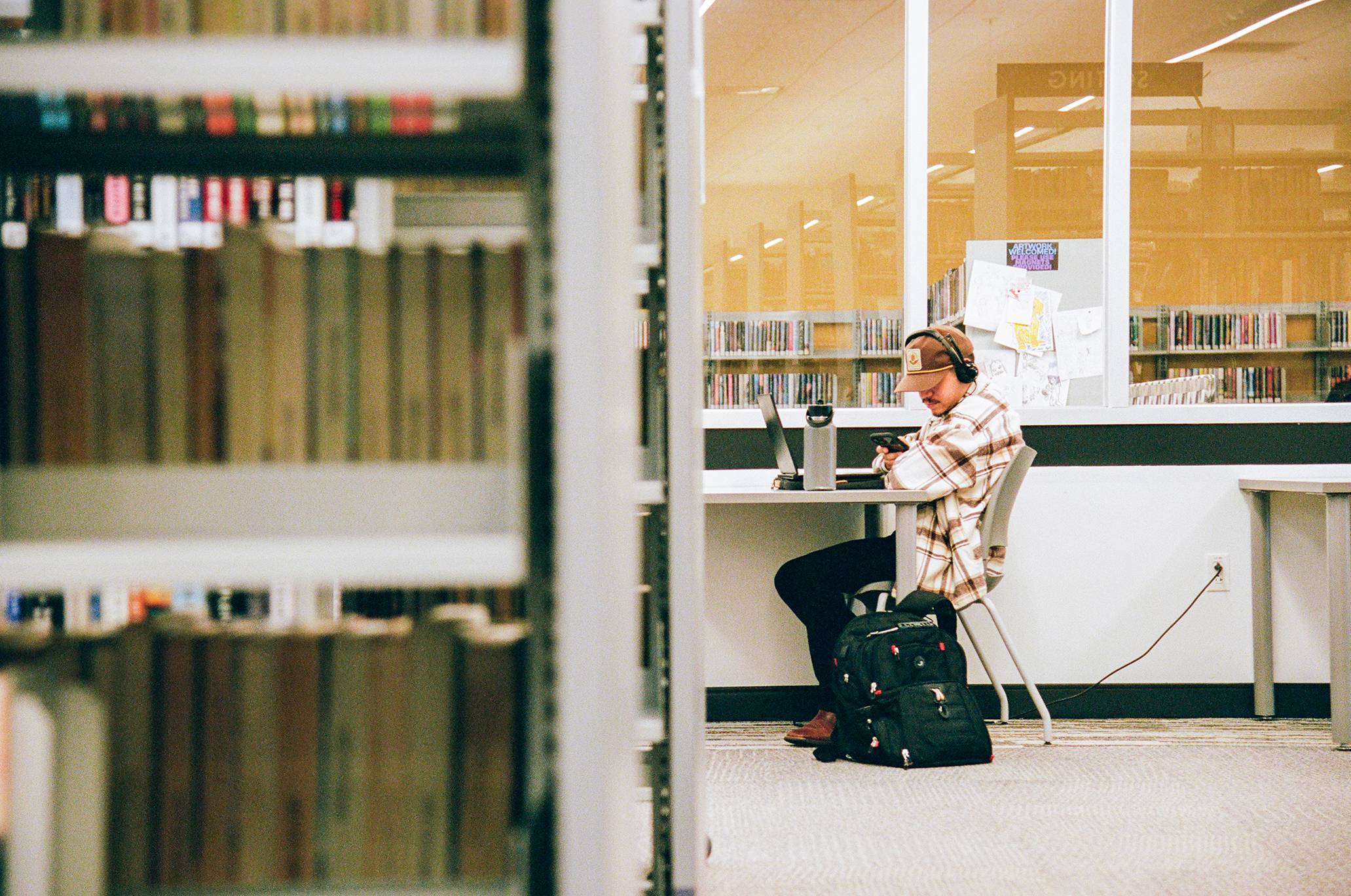 man sits at a table working at a library with a row of books in the foreground