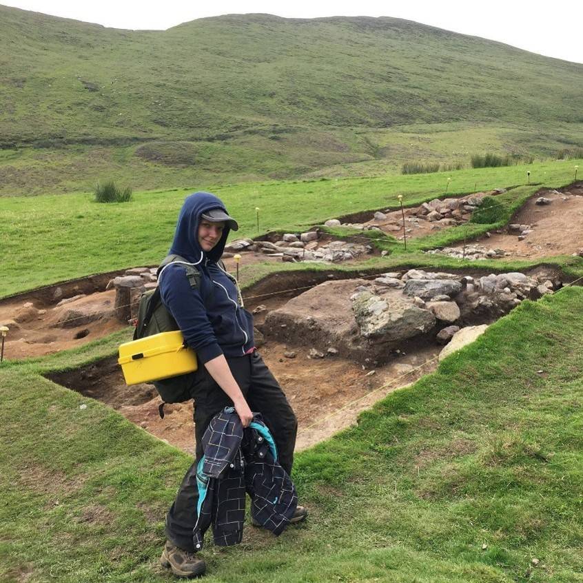 Stefanie posing in front of an archaeological site with open excavation units
