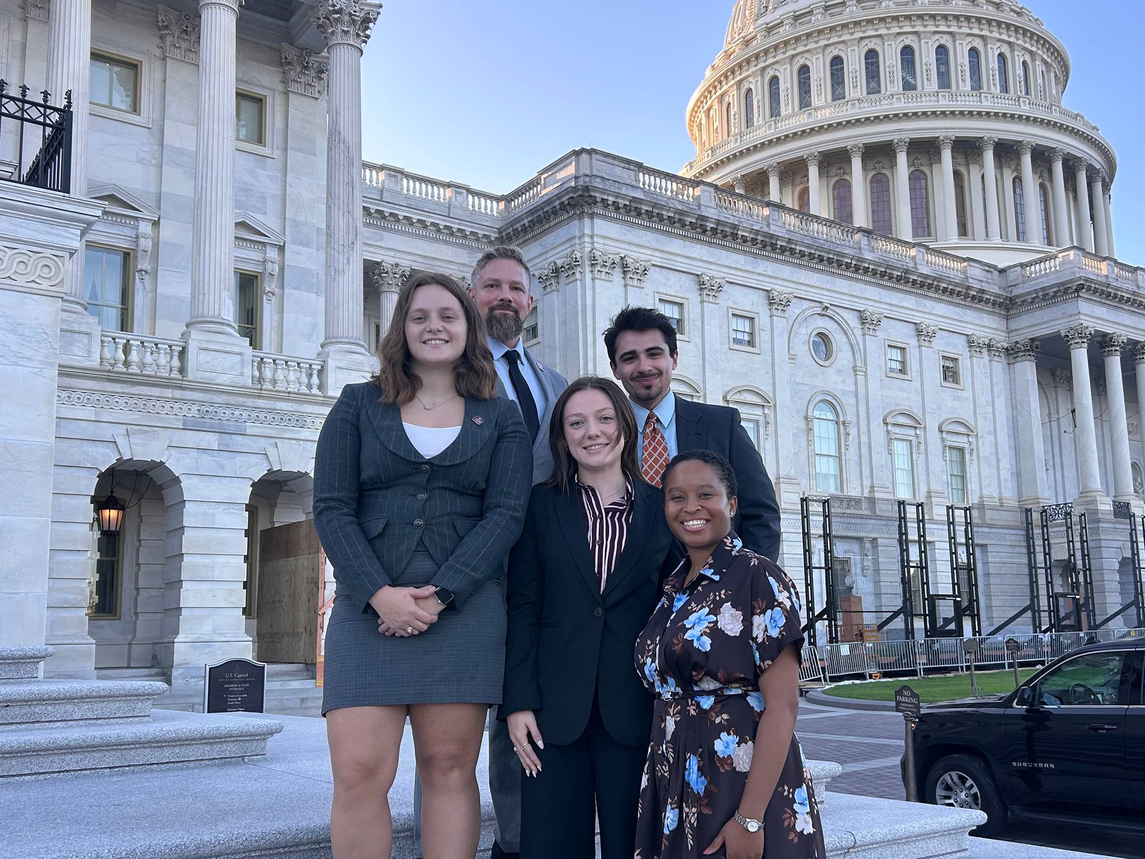 five people pose for photo on steps of the U.S. Captiol building while wearing business attire. 