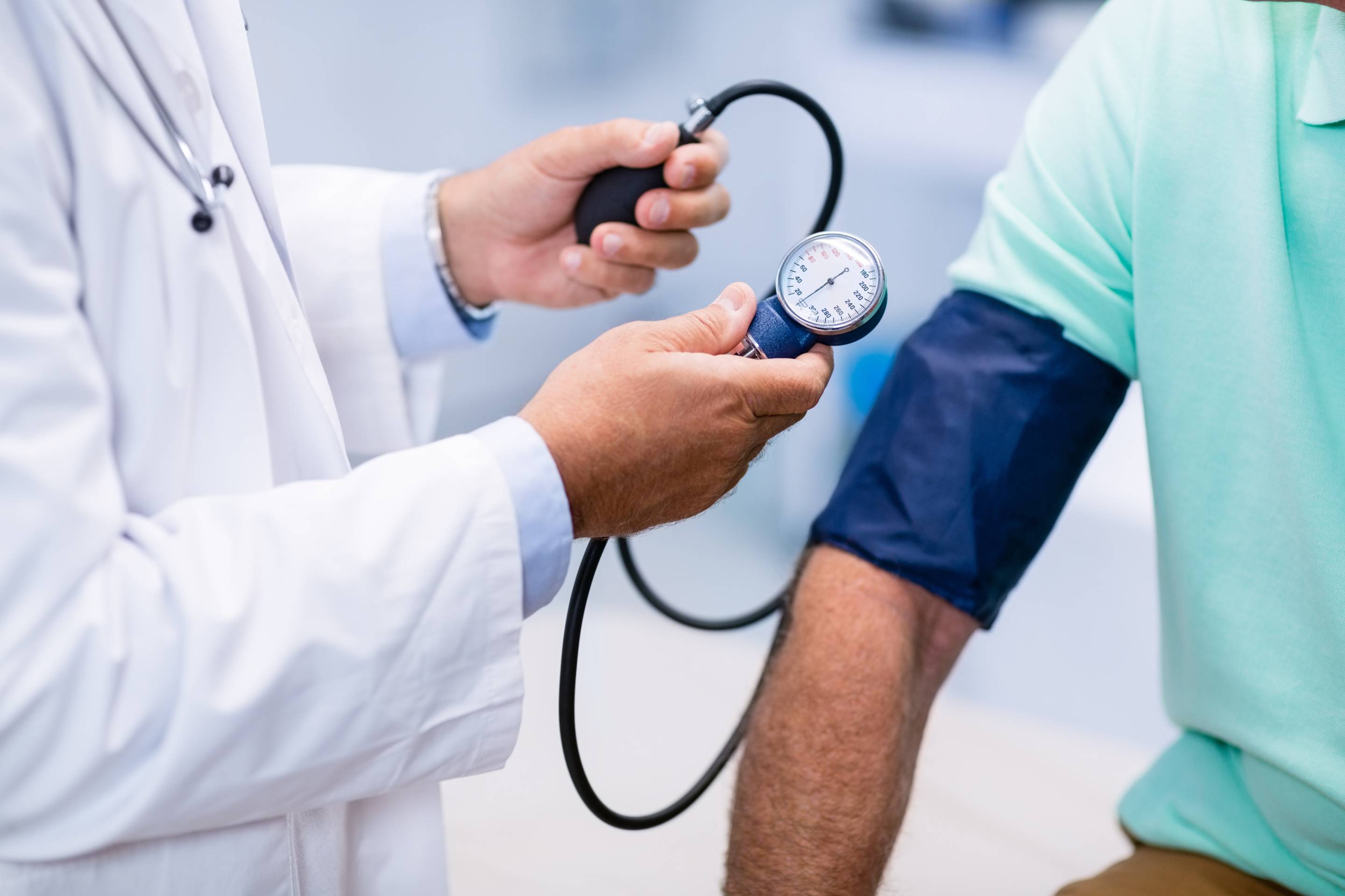 Healthcare professional measuring a patient’s blood pressure with an upper-arm cuff, hand pump, and analog gauge