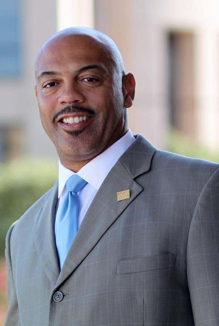 Outdoors headshot of Dr. Vincent E. Morton wearing a grey suit with a light blue tie