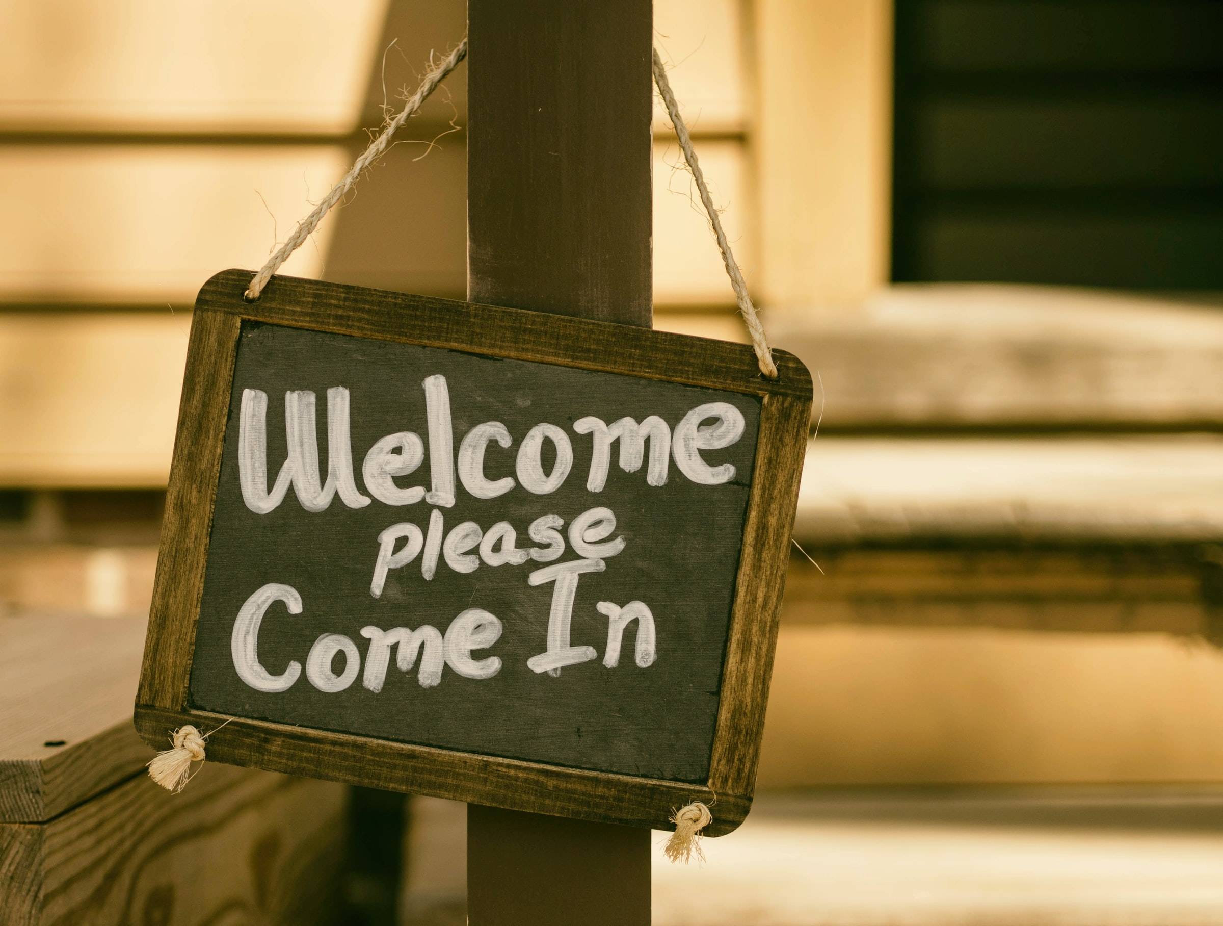 A hanging chalkboard sign that says "Welcome please come in."