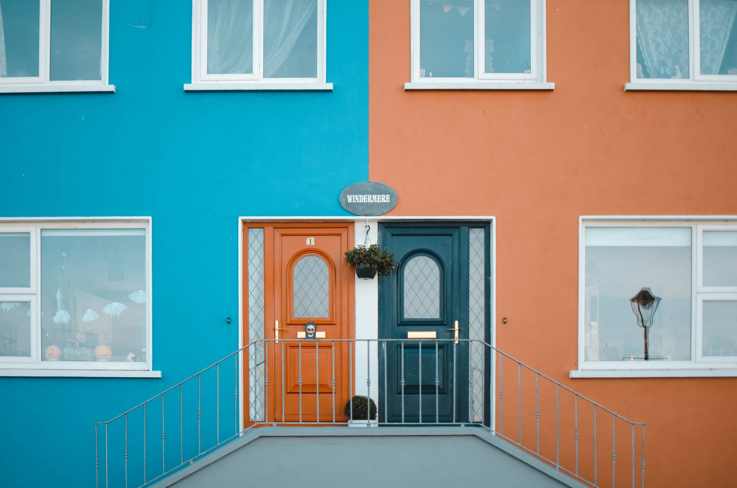 Photograph of a duplex. One side is cyan the other is orange. The front doors match the other's color theme.